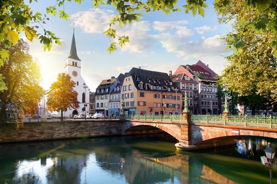Straßburger Altstadt mit Fachwerkhäusern und Kanälen, umgeben von grünen Bäumen, unter blauem Himmel.