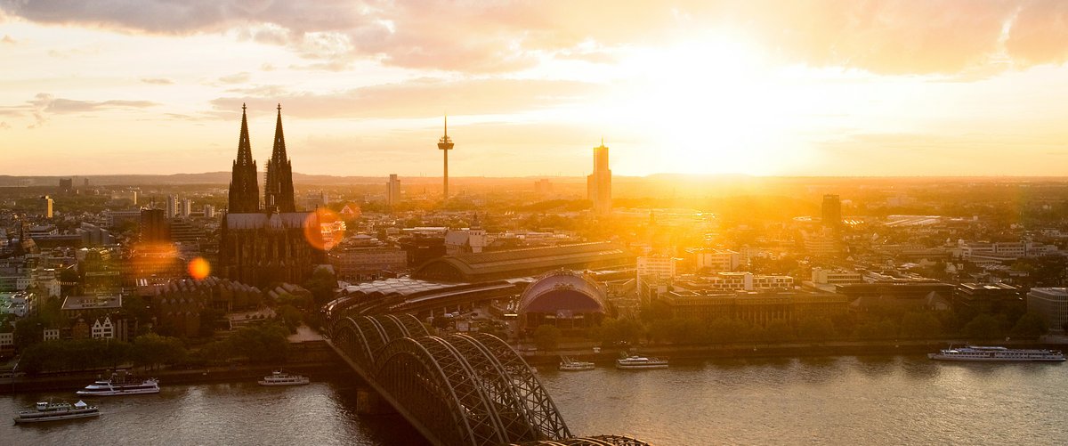 Panoramablick auf die Stadt Köln mit dem Kölner Dom bei Sonnenuntergang. Im Vordergrund die Hohenzollernbrücke, die über den Rhein führt.