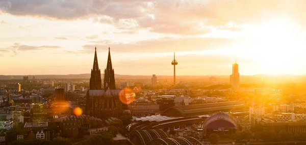 Panoramablick auf die Stadt Köln mit dem Kölner Dom bei Sonnenuntergang. Im Vordergrund die Hohenzollernbrücke, die über den Rhein führt.