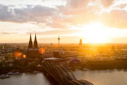Panoramablick auf die Stadt Köln mit dem Kölner Dom bei Sonnenuntergang. Im Vordergrund die Hohenzollernbrücke, die über den Rhein führt.