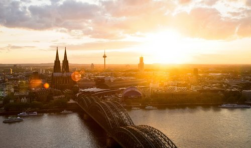 Panoramablick auf die Stadt Köln mit dem Kölner Dom bei Sonnenuntergang. Im Vordergrund die Hohenzollernbrücke, die über den Rhein führt.