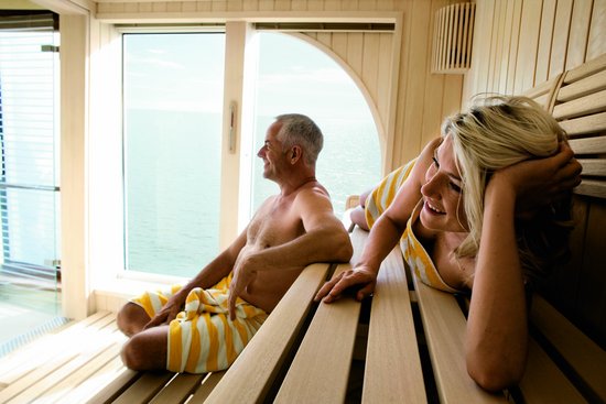 Zwei Personen entspannen in der modernen Sauna mit Holzbänken und einem großen Fenster, das einen Blick auf die umliegende Natur bietet.