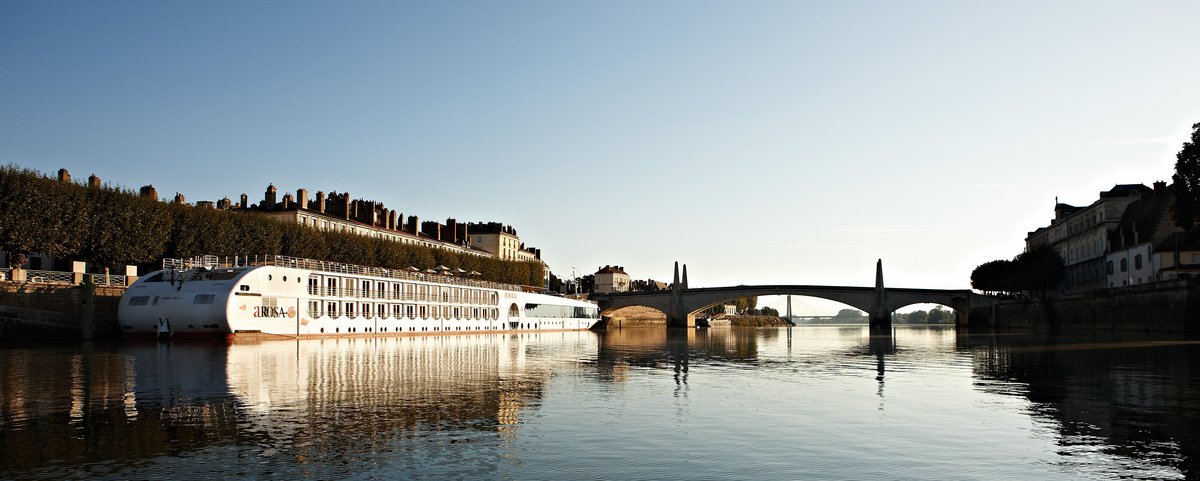 Die A-ROSA STELLA liegt am Ufer in einer Stadt an der Rhône bei Sonnenaufgang, im Hintergrund eine Brücke und Gebäude. 