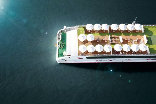 Draufsicht auf das Sonnendeck des Flusskreuzfahrtschiffs A-ROSA mit weißen Sonnenschirmen und Tischen auf dem Wasser.