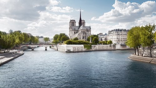 Blick auf die Kathedrale Notre-Dame de Paris von der Seine aus mit Brücken, Bäumen und historischen Gebäuden bei bewölktem Himmel.