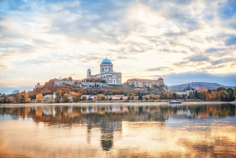 Blick auf die Basilika von Esztergom, Ungarn, mit grüner Kuppel und Donau im Vordergrund, umgeben von herbstlich bunter Landschaft.