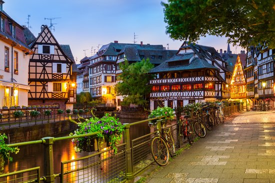 Straßburger Altstadt mit Fachwerkhäusern umgeben von Bäumen und einem Fluss bei Abenddämmerung.