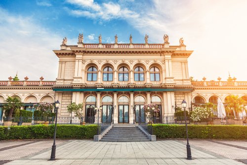 Beigefarbene Frontfassade eines barocken Gebäudes in Wien. Die Sonne strahlt golden über die Fassade hinweg.