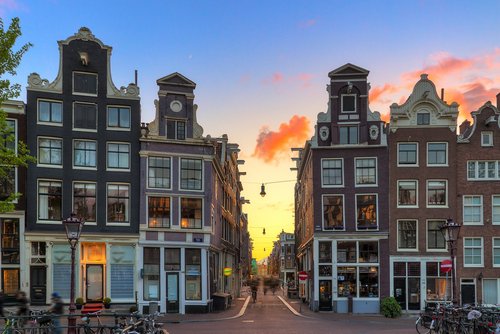 Eine Gasse mit historsichen Gebäuden in Amsterdam bei Sonnenuntergang. Fahrradfahrer fahren durch die Gasse